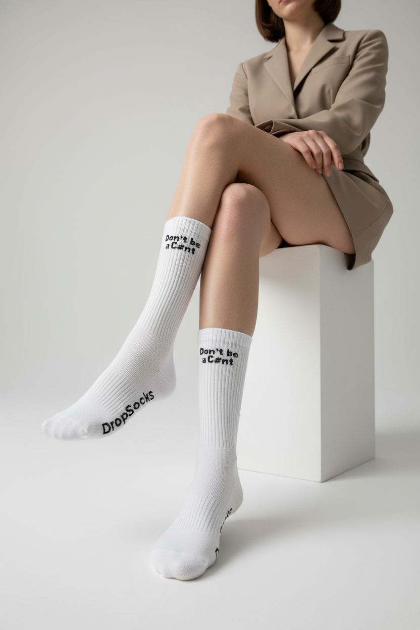 Person wearing white socks with text, sitting on a white cube against a plain background